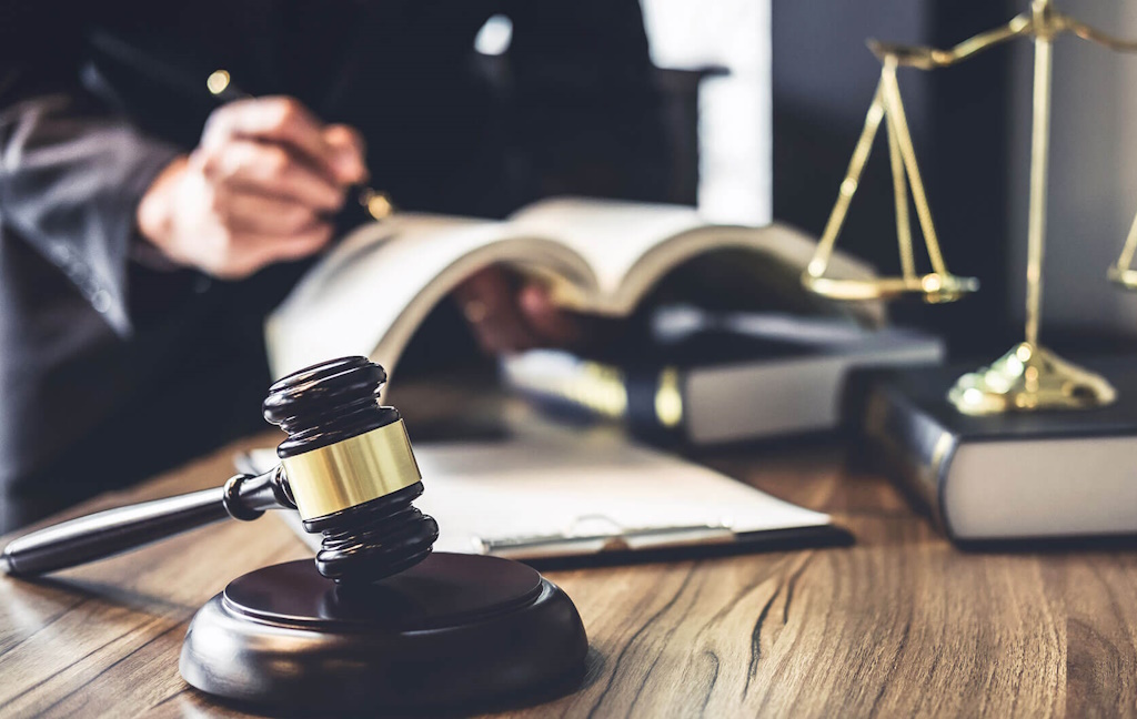 Courtroom objects such as a gavel, balance, books, and someone inspecting and writing in the book